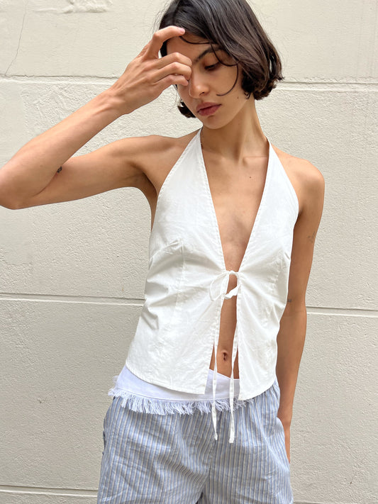 female model wears the open halter top top by Deiji Studios in white

top features open front with centre bust tie, halter neck tie and v neckline, bust seams for subtle shaping and shirred back

made from 100% GOTS certified organic cotton poplin

paired with a blue stripe cotton short