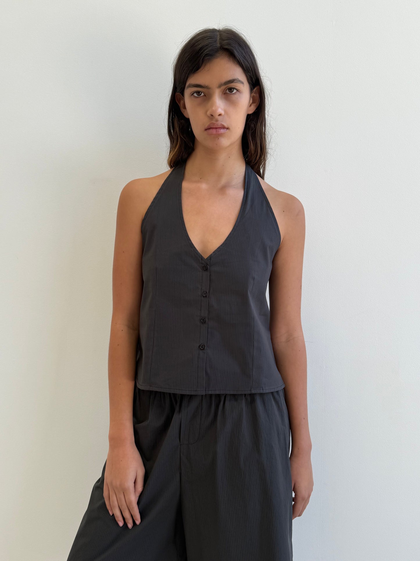 A woman with long dark hair wears the Deiji Studios Waist Halter - Black Stripe with matching loose pants, standing against a plain white wall.
