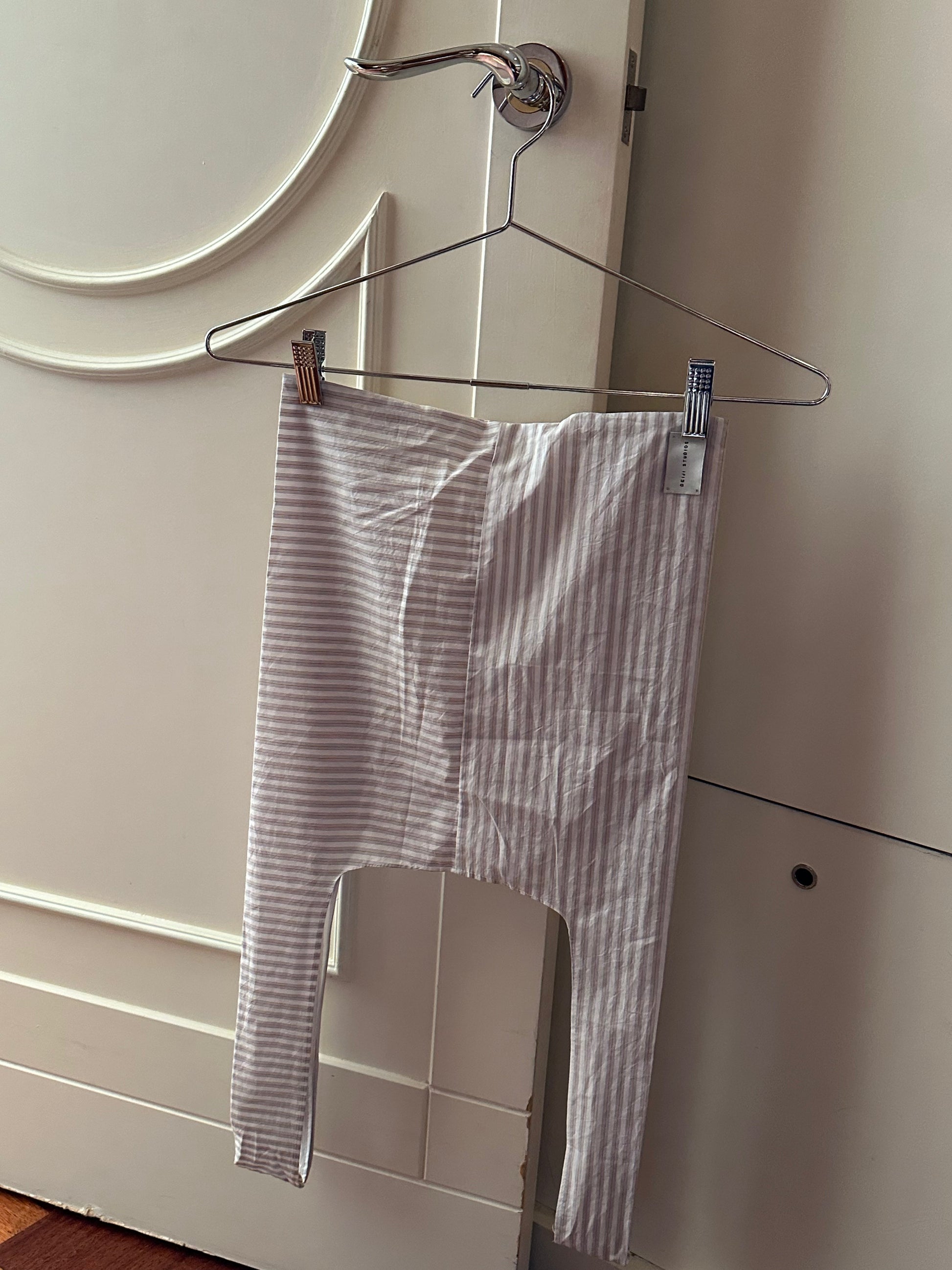 A Seam Tote in Lake Stripe from Deiji Studios hangs from a metal hanger on a door handle in a softly lit room.