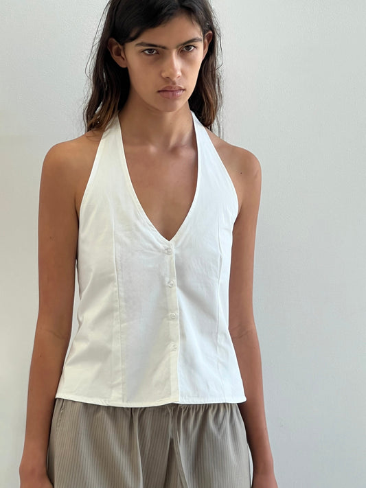 A person with long brown hair wears Deiji Studios Waist Halter - White top, paired with light gray pleated pants, standing against a plain light-colored background.