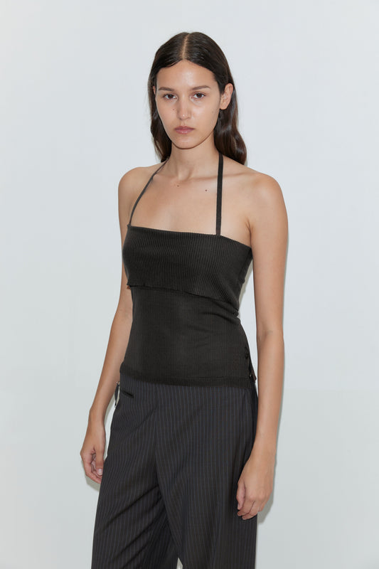 A woman with long brown hair stands against a plain white background with a neutral expression, wearing the Half Top - Black and pinstriped pants.