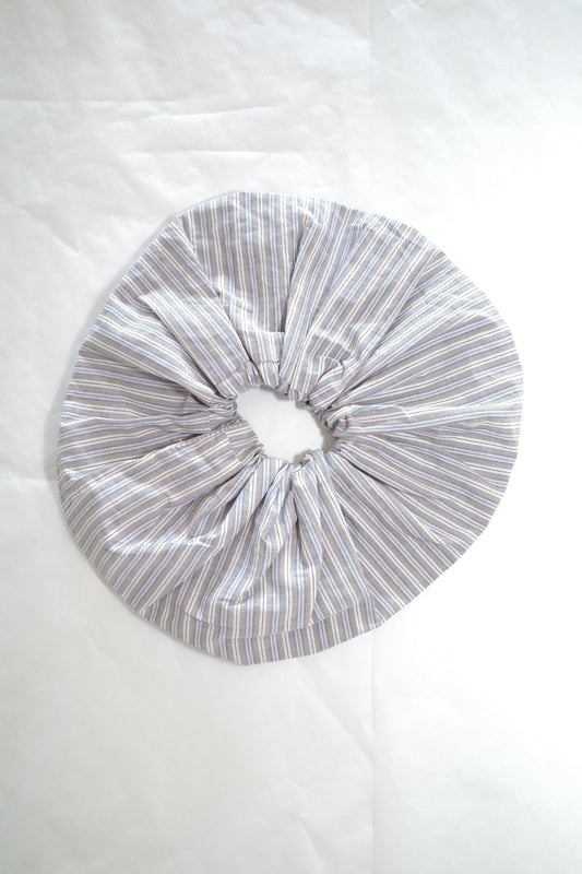 A large scrunchie made from light-colored fabric with thin blue and white stripes, shown on a white background.
