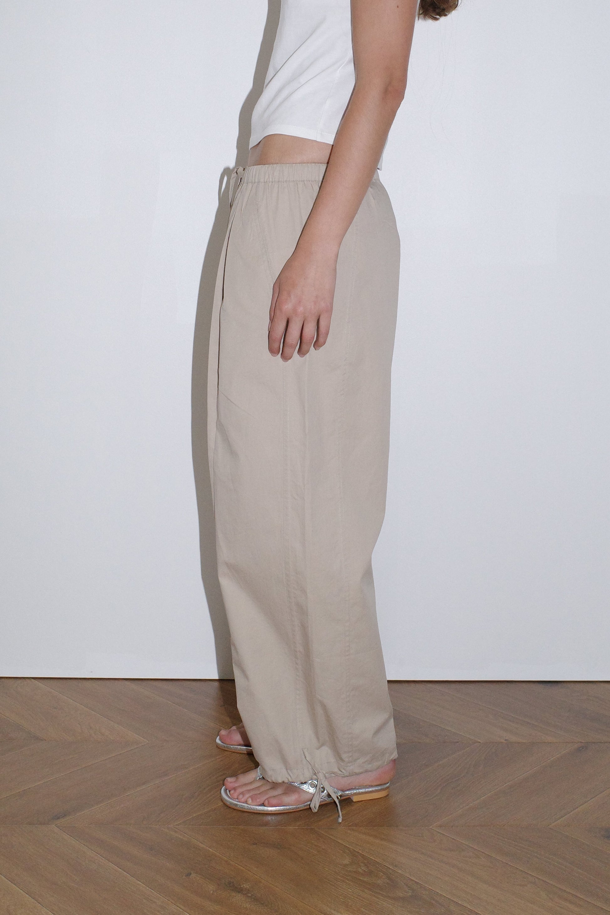 female model wears beige soft cotton trouser featuring a drawcord hem and waist with deep side pockets designed to sit mid-low waist for a relaxed look and made from 100% GOTS certified organic cotton.