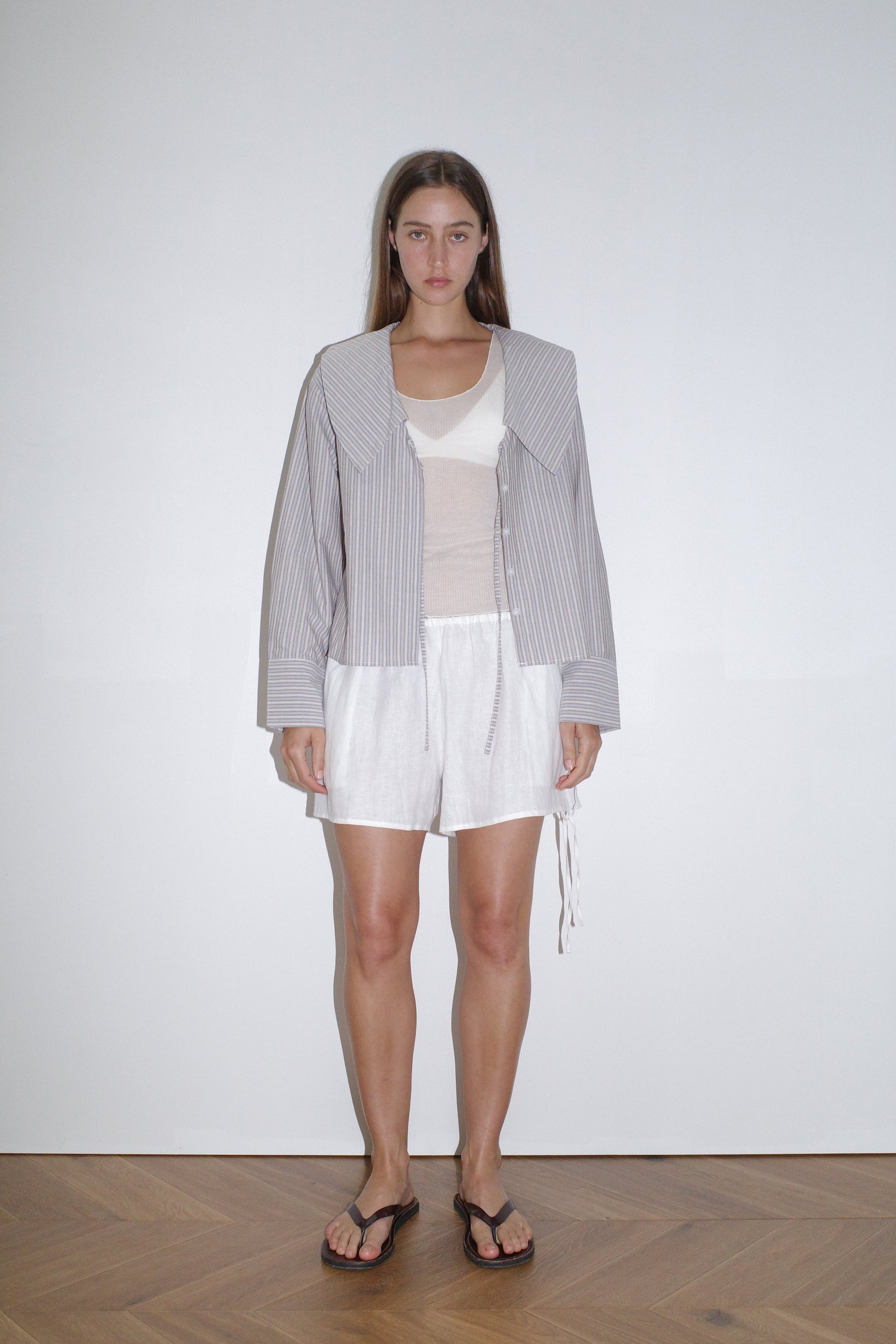 female model wears the collared tie shirt by Deiji Studios in seas stripe


a structured shirt features an oversized collar and cuff, tie at front collar opening, dropped shoulder and elongated sleeves in a boxy fit


made from 100% GOTS certified organic cotton poplin

paired with a knit tank in off white and white linen short