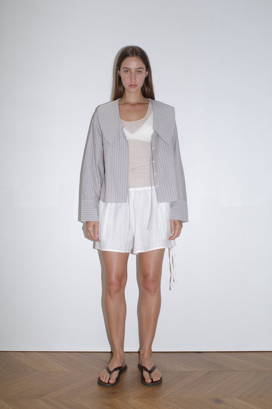 female model wears the collared tie shirt by Deiji Studios in seas stripe


a structured shirt features an oversized collar and cuff, tie at front collar opening, dropped shoulder and elongated sleeves in a boxy fit


made from 100% GOTS certified organic cotton poplin

paired with a knit tank in off white and white linen short