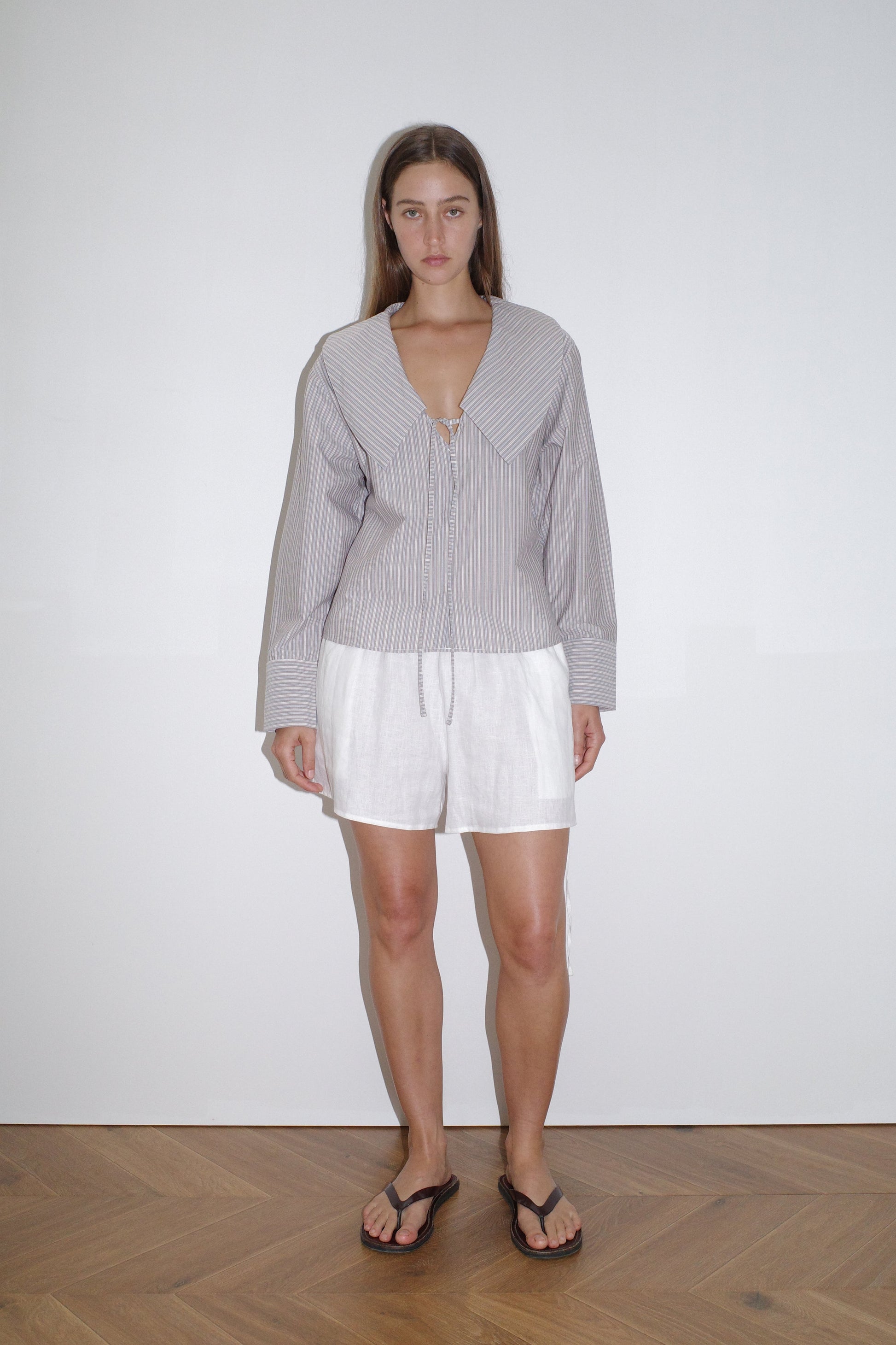 female model wears the collared tie shirt by Deiji Studios in seas stripe


a structured shirt features an oversized collar and cuff, tie at front collar opening, dropped shoulder and elongated sleeves in a boxy fit


made from 100% GOTS certified organic cotton poplin

paired with a white linen short