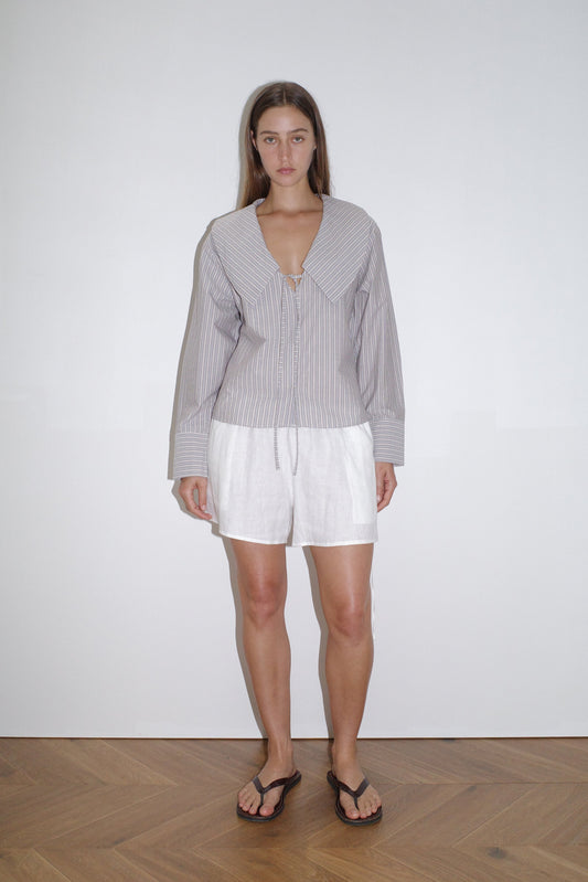 female model wears the collared tie shirt by Deiji Studios in seas stripe


a structured shirt features an oversized collar and cuff, tie at front collar opening, dropped shoulder and elongated sleeves in a boxy fit


made from 100% GOTS certified organic cotton poplin

paired with a white linen short