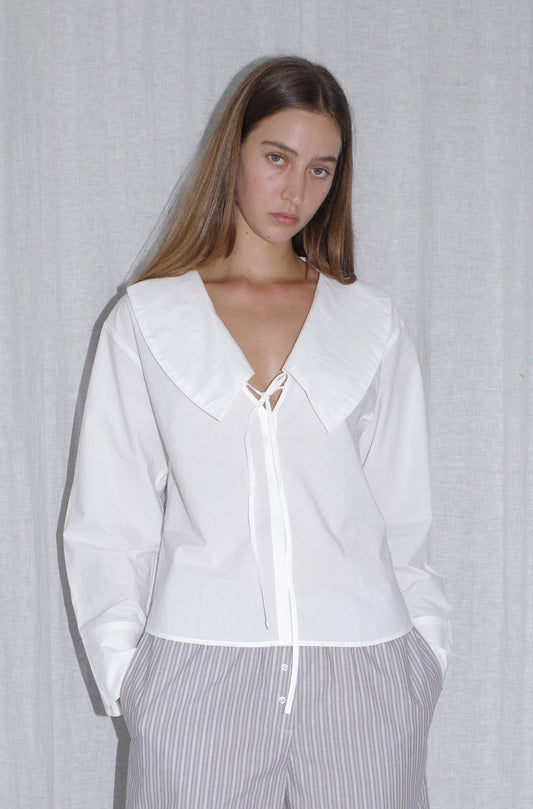 female model wears the collared tie shirt by Deiji Studios in white


a structured shirt features an oversized collar and cuff, tie at front collar opening, dropped shoulder and elongated sleeves in a boxy fit


made from 100% GOTS certified organic cotton poplin

paired with a blue stripe boxer