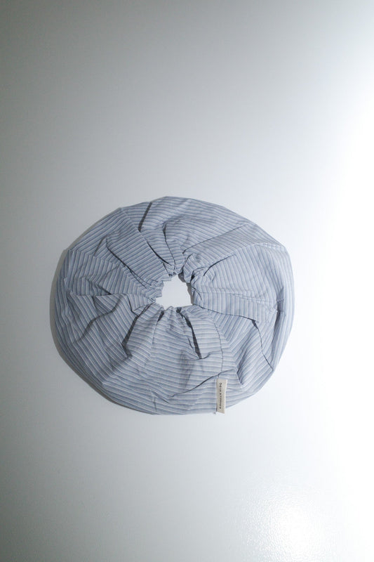 The Scrunchie - Sky Stripe from Deiji Studios, made of oversized organic cotton in light blue and white stripes, is arranged in a circular shape on a plain white surface.