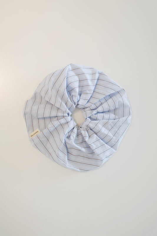 The Scrunchie - Mineral Stripe is a voluminous, oversized light blue cotton scrunchie with brown pinstripes, a gathered circular design, and a small Deiji Studios branded label, shown laid flat on a white surface.