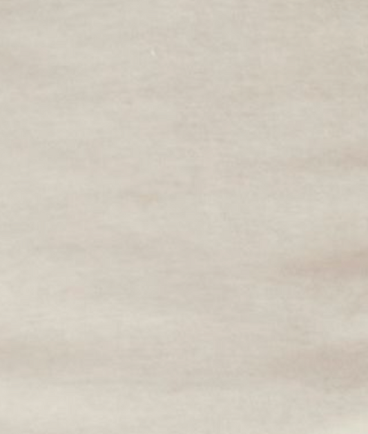 A close-up of the Flounce Tee - Cream reveals a smooth, light beige surface with subtle, natural variations and delicate lines, echoing minimalist style and the refined texture of a fitted tee.