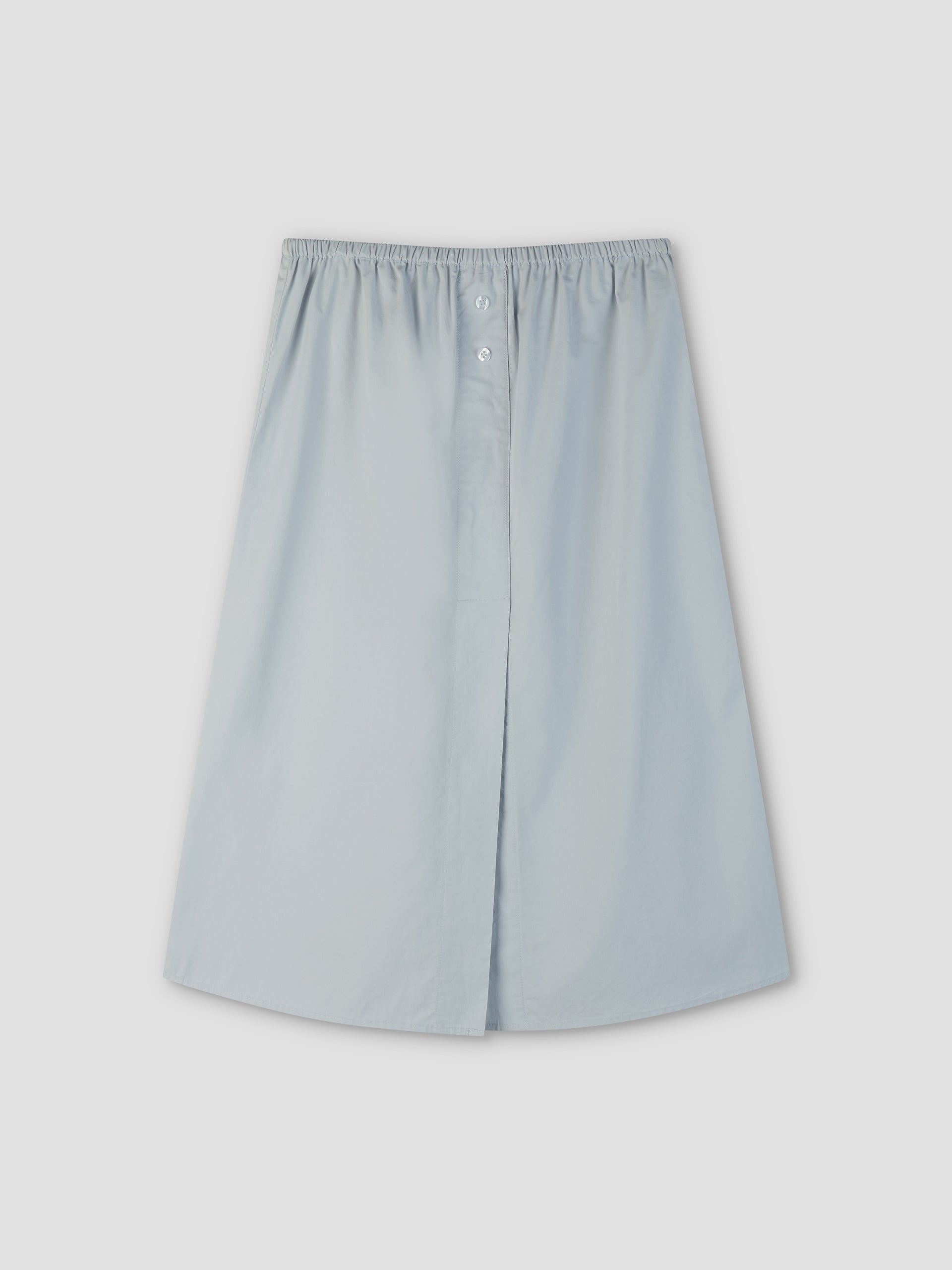 The Overlap Skirt - Blue by Deiji Studios is a light blue, knee-length A-line skirt with an elastic waistband and front button detail, shown on a plain light gray background.