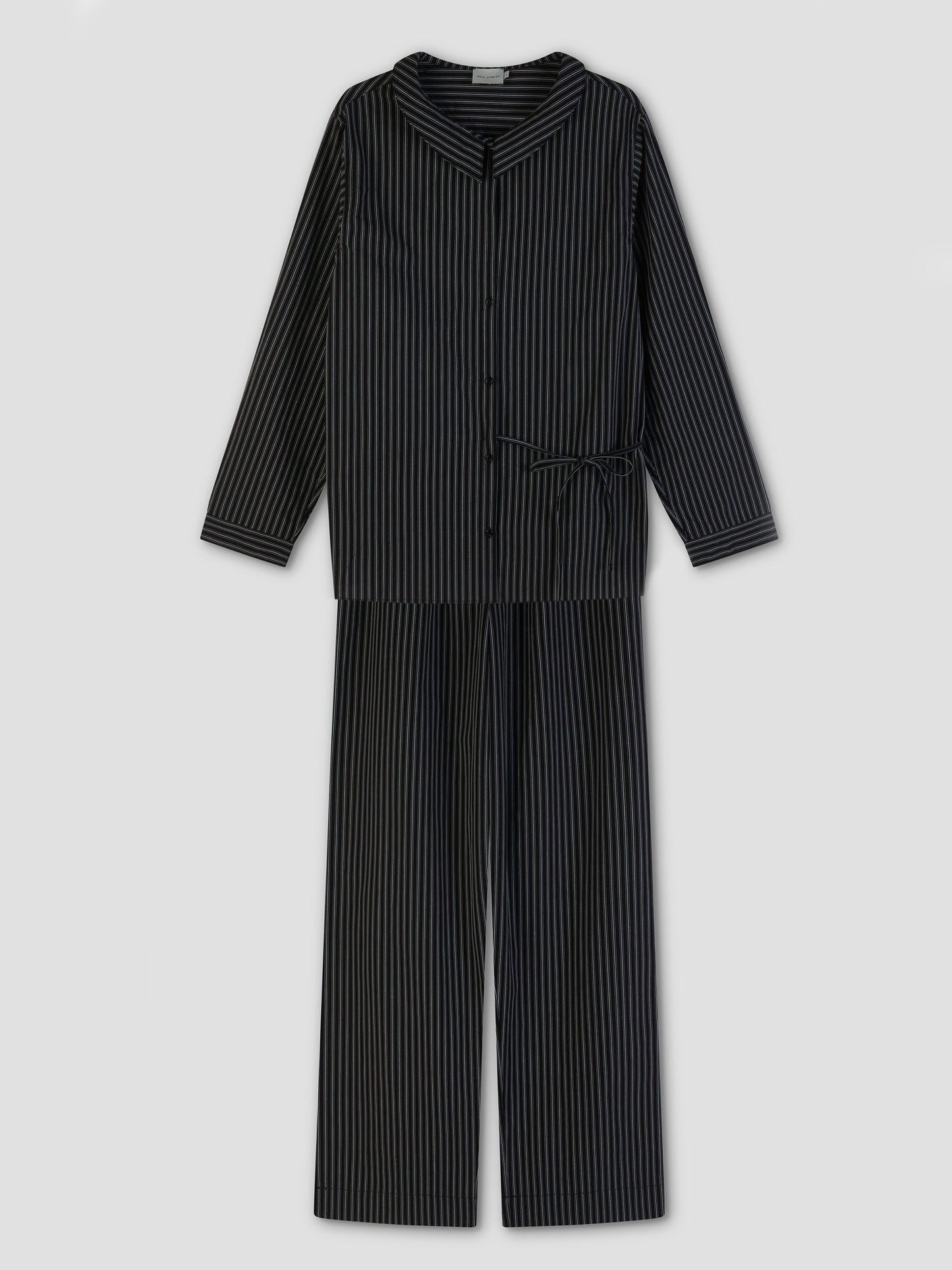The Left Set - Mono Stripe features black pajamas with thin white stripes, including a lightweight, relaxed-fit long-sleeve button-up shirt and matching pants, displayed flat on a light gray background.