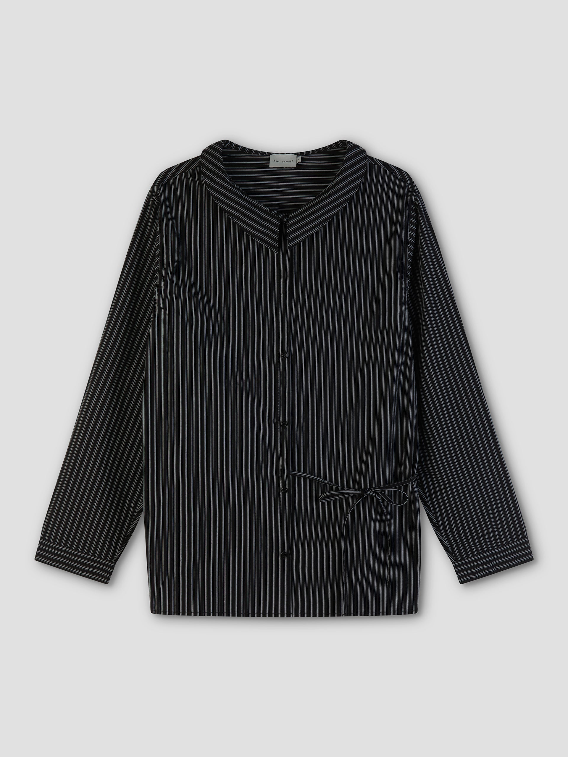 The Left Shirt is a black long-sleeve button-up with thin white vertical stripes, a wide collar, and a small side bow at the waist, shown laid flat on a plain gray background.