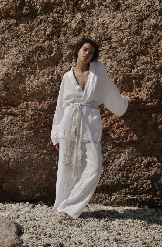 Wearing the 01 Set, a person stands relaxed against a rocky wall on a pebble-covered ground, with one hand resting on the rock and the other by their side.
