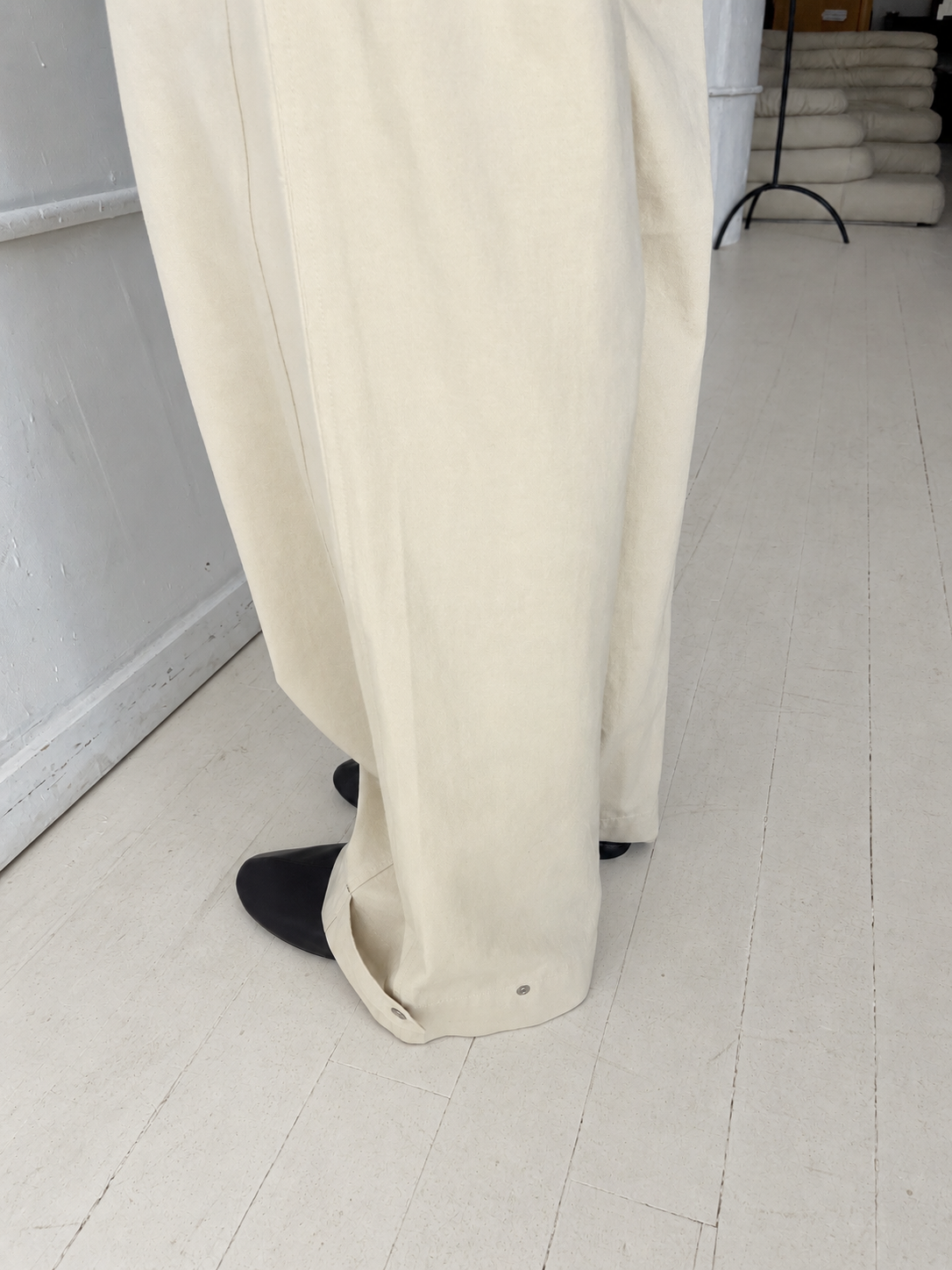 A close-up of the Snap Tab Pant - Stone by Deiji Studios, showing the wide-leg hem with its adjustable snap tab, worn with black shoes.