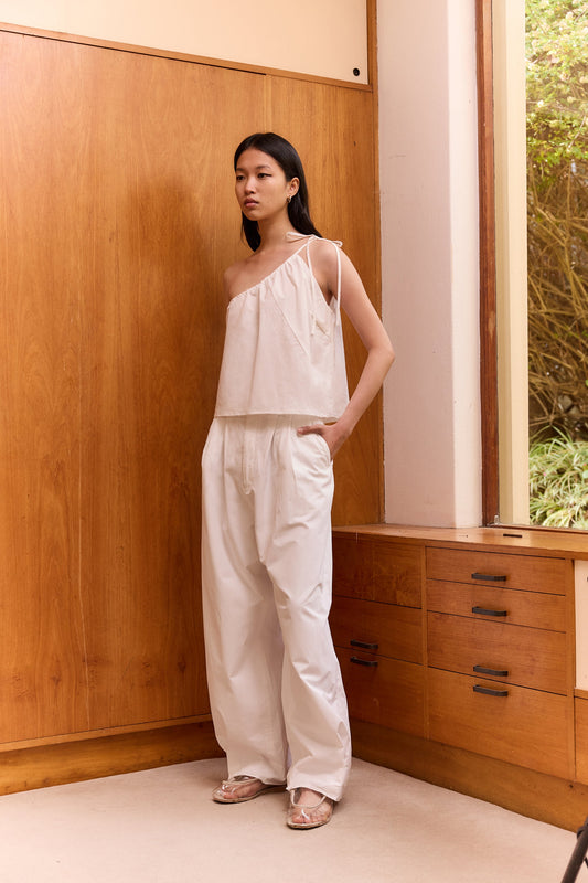 A woman with long straight hair stands indoors by a wooden wall and large window, wearing the off-white Multi Strap Top and matching wide-leg pants, paired with neutral sandals.
