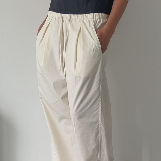 female model wears off white soft cotton trouser featuring a drawcord hem and waist with deep side pockets designed to sit mid-low waist for a relaxed look and made from 100% GOTS certified organic cotton. Paired with the asymmetric tie top  in ink, an elevated asymmetric top with a softly gathered front neckline and elastic neckline. Made from 100% GOTS certified organic, OEKO-TEX 100 certified and EU certified stone washed french linen.