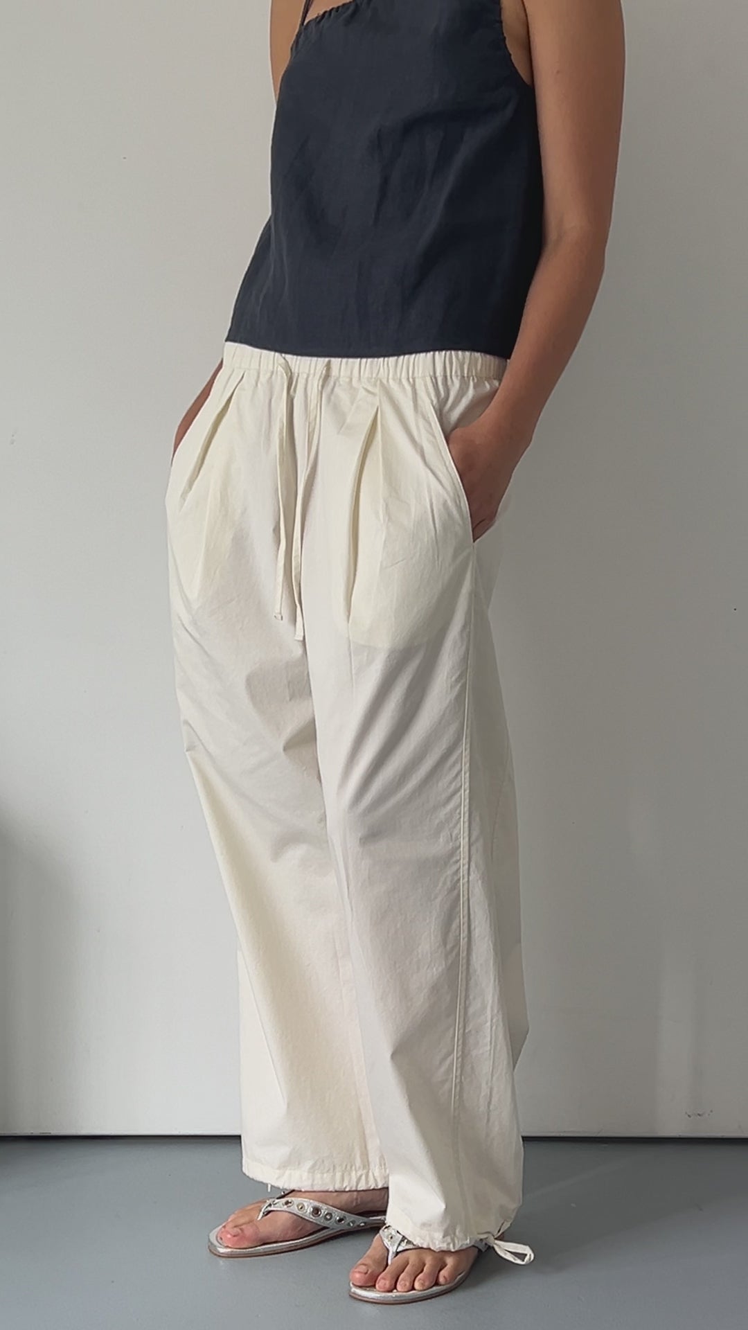 female model wears off white soft cotton trouser featuring a drawcord hem and waist with deep side pockets designed to sit mid-low waist for a relaxed look and made from 100% GOTS certified organic cotton. Paired with the asymmetric tie top  in ink, an elevated asymmetric top with a softly gathered front neckline and elastic neckline. Made from 100% GOTS certified organic, OEKO-TEX 100 certified and EU certified stone washed french linen.