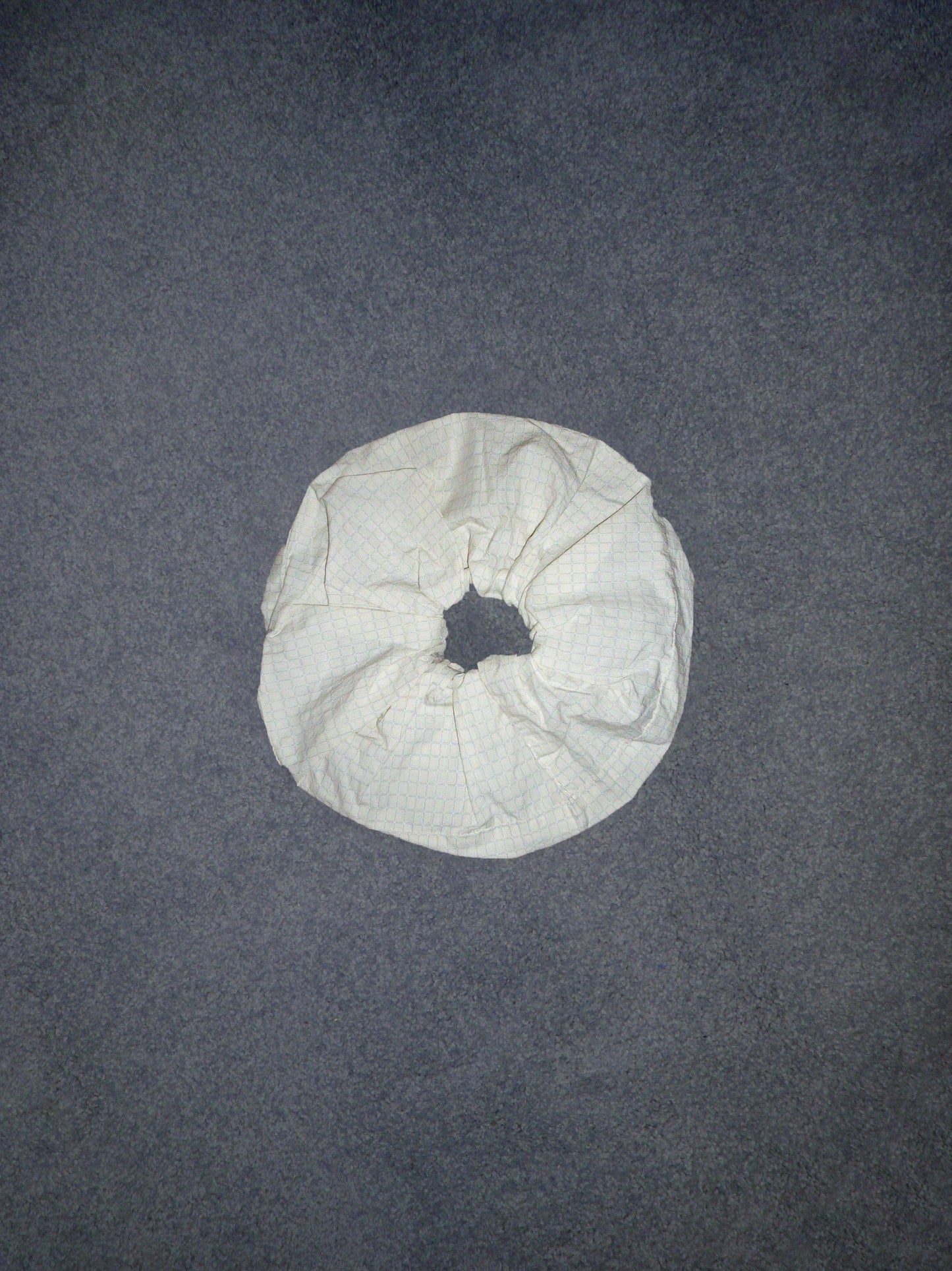 A Scrunchie made of white, crumpled fabric rests on a gray textured surface, shown from above.