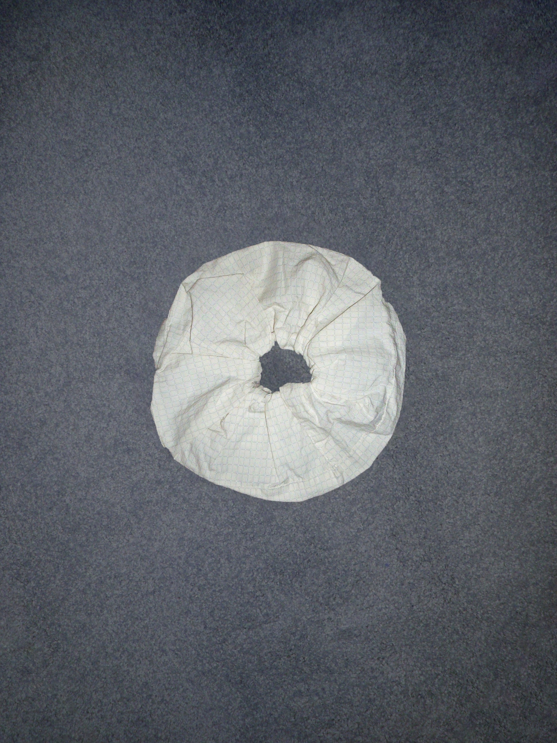 A Scrunchie made of white, crumpled fabric rests on a gray textured surface, shown from above.