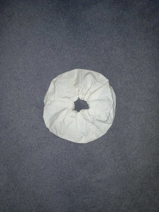 A Scrunchie made of white, crumpled fabric rests on a gray textured surface, shown from above.