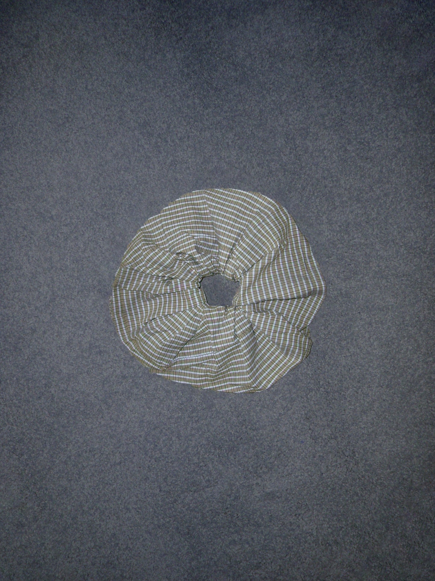 A Deiji Studios Scrunchie featuring green, blue, and white plaid fabric rests on a flat, dark gray surface.