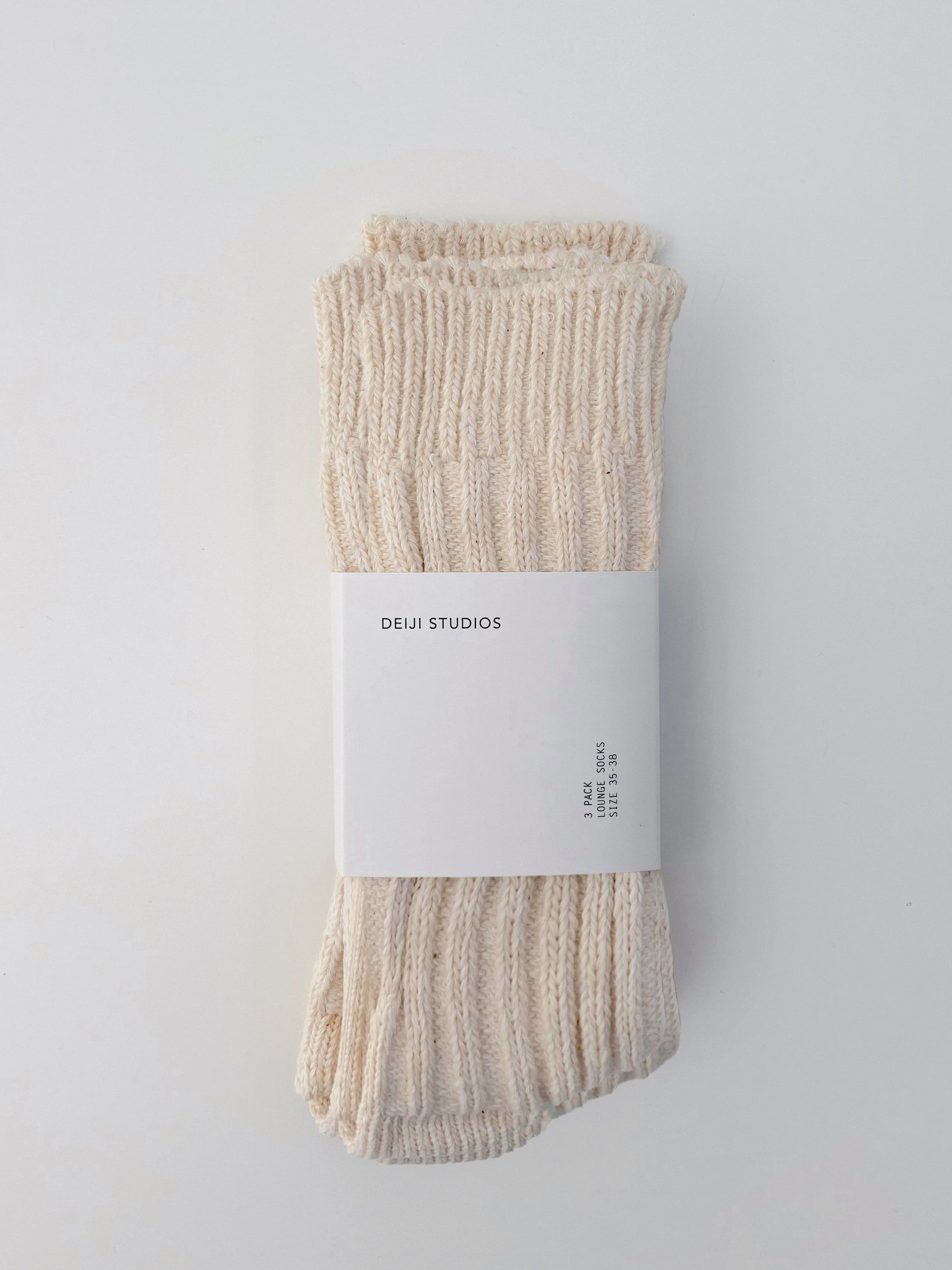A pair of cream-colored, ribbed knit Woven Socks folded together with a white paper label showing the Deiji Studios brand, set against a plain white background.